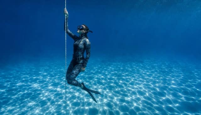 A freediver hanging on the line above a pale, rippled sandy seabed.