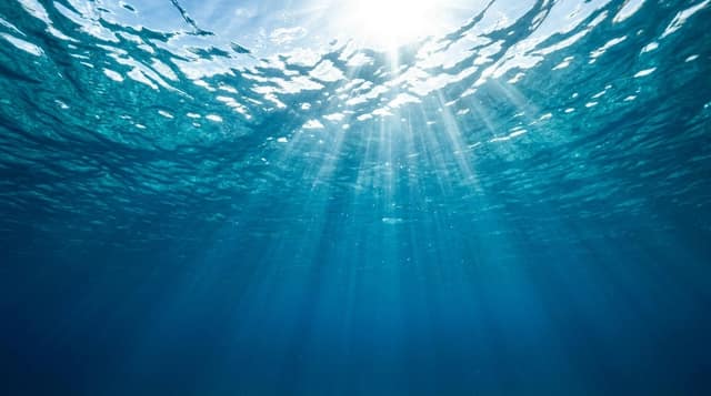 Sunlight fanning down through the rippled surface into open blue water.